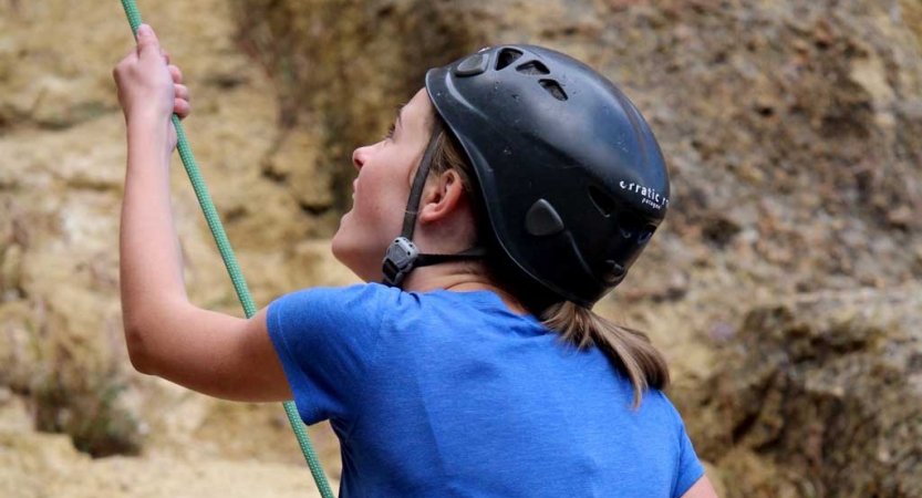 A person wearing a helmet holds onto a rope as they belay a climber.